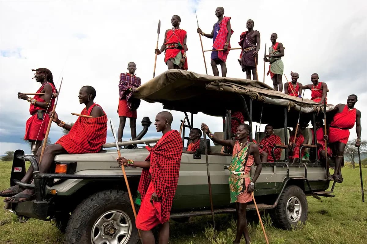 Group of Maasai men in red shukas standing on and around a safari vehicle