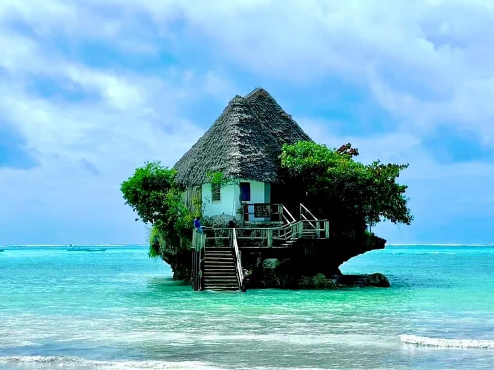 Thatched restaurant on a rock in turquoise water off Zanzibar